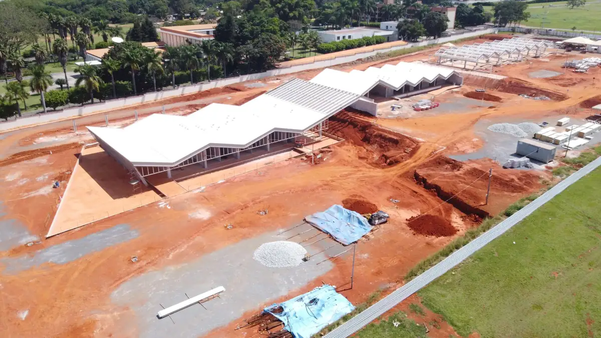 Vista aérea aproximada da estrutura metálica montada, com a treliça da cobertura visível antes do fechamento