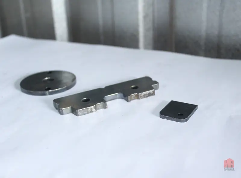 Conjunto de três peças cortadas: um disco, uma barra furada e uma placa quadrada